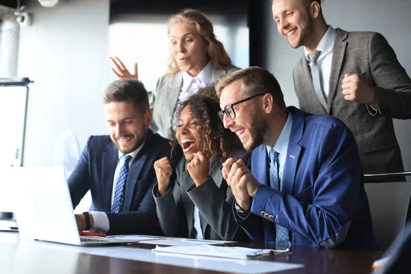 幸せなビジネスの人々はオフィスのノートパソコンの近くで笑う。成功したチームの同僚は冗談を言い、仕事で一緒に楽しみます. — ストック写真