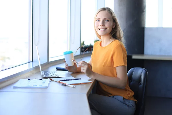 Mulher de negócios sorridente bonita está sentada no escritório e olhando para a câmera — Fotografia de Stock