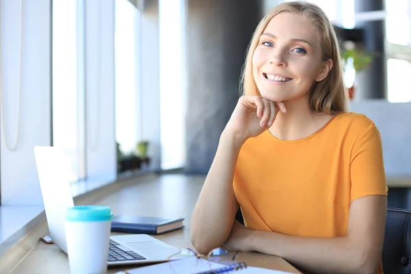 Mulher de negócios sorridente bonita está sentada no escritório e olhando para a câmera — Fotografia de Stock