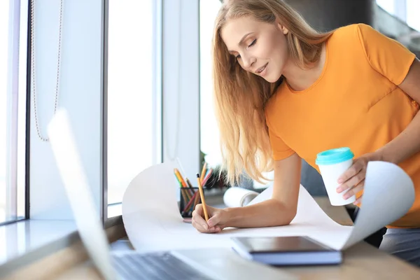 Mulher moderna bonita está escrevendo algo no plano enquanto trabalhava no escritório criativo — Fotografia de Stock