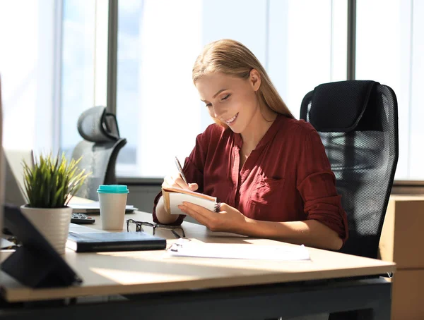 Hermosa mujer de negocios está escribiendo algo mientras está sentada en el escritorio de la oficina — Foto de Stock