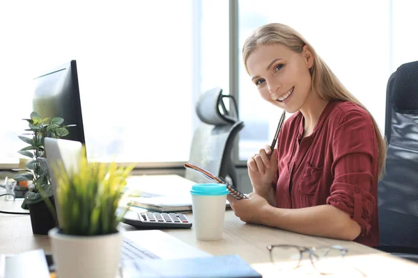 Mulher de negócios sorridente bonita está sentada no escritório e olhando para a câmera — Fotografia de Stock