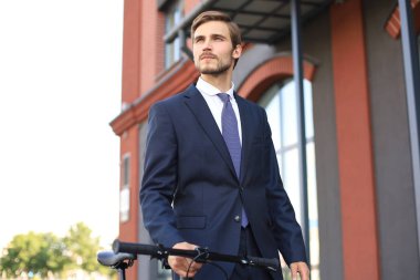 Bir şehir caddesinde bisikletle yürürken takım elbise giymiş genç şık iş adamı.