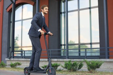Şehir caddesinde elektrikli scooter kullanan genç iş adamı. Modern ve ekolojik ulaşım konsepti.