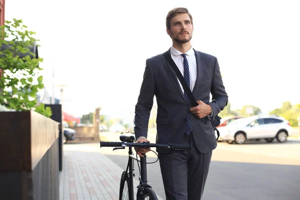街の路上で自転車で歩くペンシブな若いビジネスマン. — ストック写真