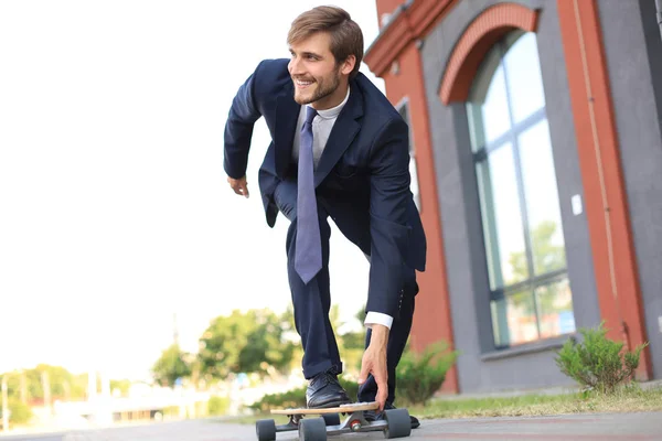 Giovane uomo d'affari sicuro in giacca e cravatta a longboard che si affretta al suo ufficio, per strada in città . — Foto Stock