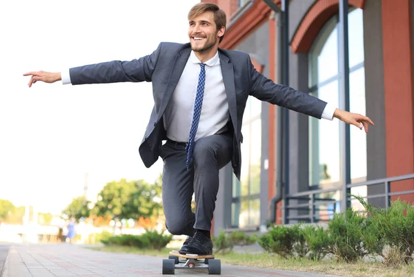 Giovane uomo d'affari sicuro in giacca e cravatta a longboard che si affretta al suo ufficio, per strada in città . — Foto Stock