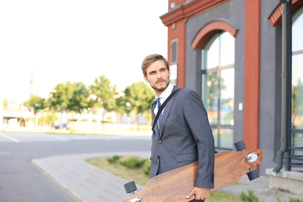 Jovem empresário confiante andando na rua, usando longboard . — Fotografia de Stock