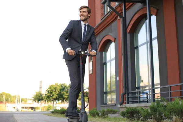 Young business man in suit riding on electric scooter on a business meeting. Ecologic transport concept.