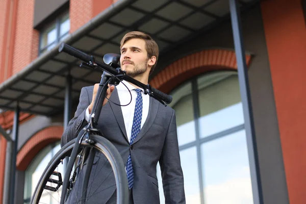 Bonito jovem empresário carregando sua bicicleta no ombro enquanto caminhava ao ar livre . — Fotografia de Stock