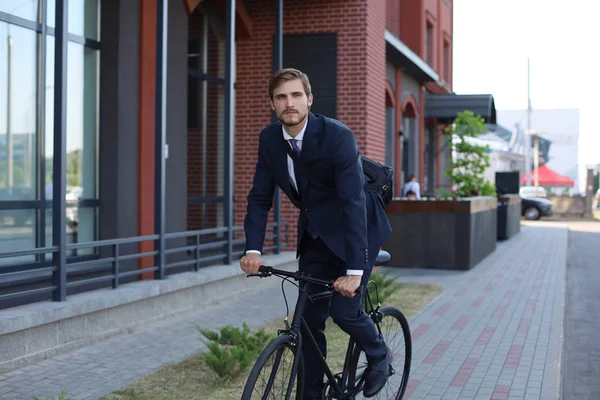 Jovem homem de negócios elegante vestido de terno andando de bicicleta em uma rua da cidade . — Fotografia de Stock