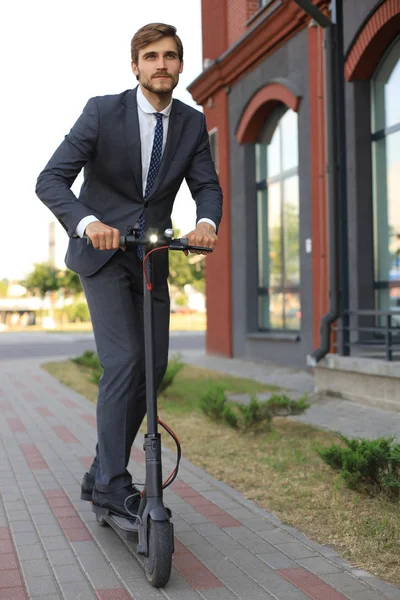 Młody człowiek biznesu w garniturze jazdy na skuterze elektrycznym na spotkaniu biznesowym. Koncepcja transportu Ecologic. — Zdjęcie stockowe