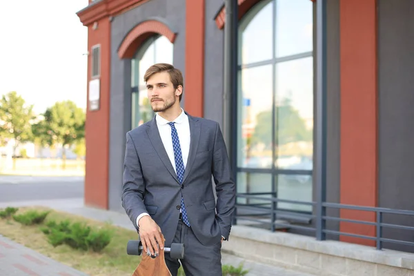 Jovem empresário confiante andando na rua, usando longboard . — Fotografia de Stock