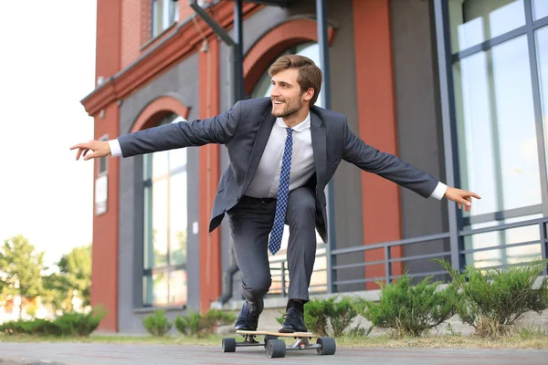 Zeker jonge zakenman in business man in pak longboard haast naar zijn kantoor, op de straat in de stad. — Stockfoto