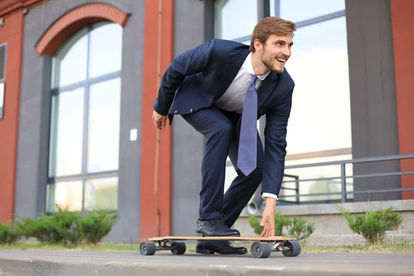 Selbstbewusster junger Geschäftsmann im Businessanzug auf Longboard eilt in sein Büro, auf der Straße in der Stadt. — Stockfoto