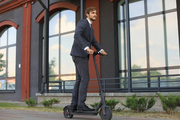 Mladý obchodní muž, který používá elektrický skútr na městské ulici. Koncepce moderního a ekologického přenosu. — Stock fotografie