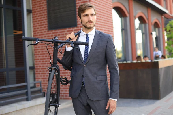 Bonito jovem empresário carregando sua bicicleta no ombro enquanto caminhava ao ar livre . — Fotografia de Stock