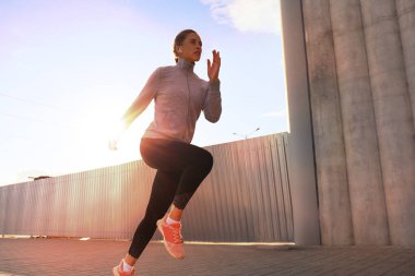 Açık havada gündoğumu veya günbatımı şehirde egzersiz yaparken çalışan genç çekici sportif fitness kadın
