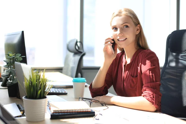 Atraktivní obchodní žena mluvit s kolegy na mobilním telefonu, zatímco sedí v kanceláři stolu — Stock fotografie