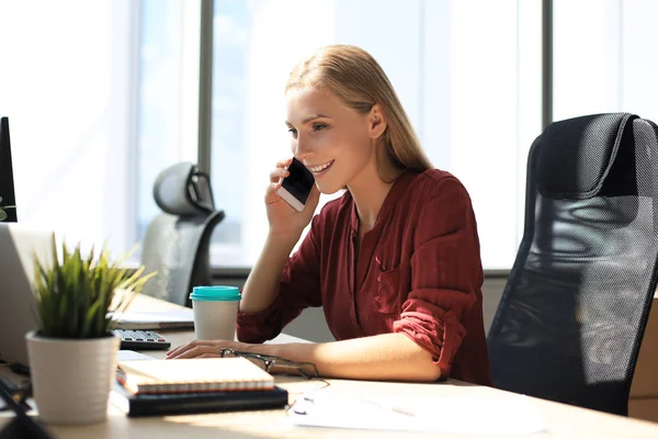 Ελκυστική επιχειρηματίας μιλάει με συναδέλφους στο κινητό τηλέφωνο, ενώ κάθεται στο γραφείο — Φωτογραφία Αρχείου