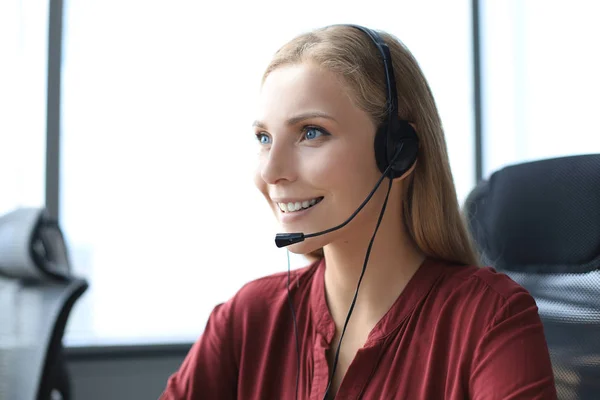 Hermosa sonriente trabajador del centro de llamadas en los auriculares está trabajando en la oficina moderna — Foto de Stock