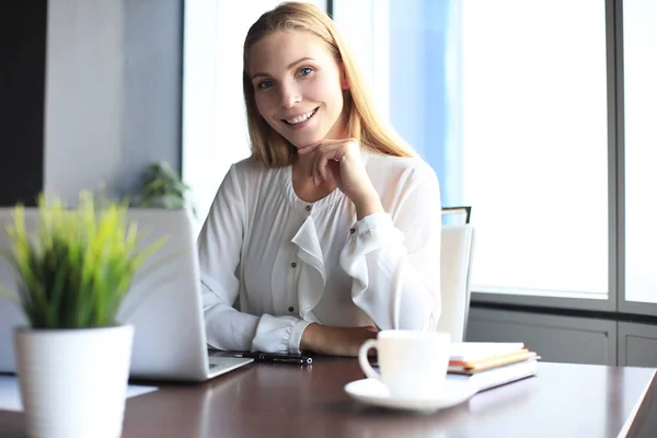 Hermosa mujer de negocios sonriente está sentada en la oficina y mirando a la cámara — Foto de Stock