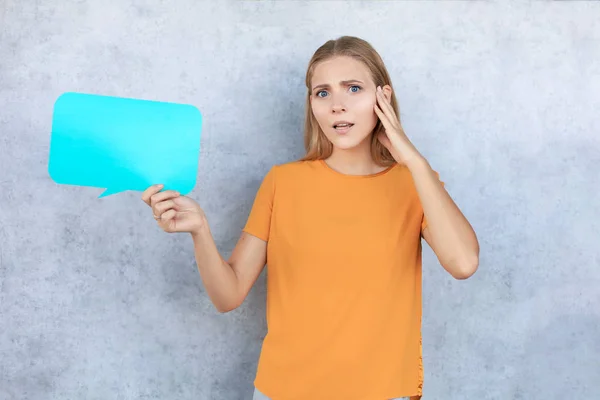 Confused young woman holding empty speech bubble isolated over grey background — Stock Photo, Image