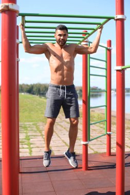 Çıplak gövdeli kaslı adam yatay çıtayı dışarı çekiyor.