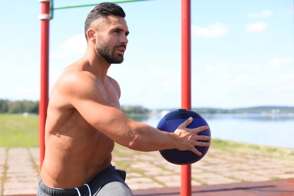 Imagen de un hombre guapo y fuerte haciendo ejercicios con una pelota de fitness al aire libre en un día soleado — Foto de Stock