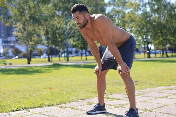 Guapo deportista con torso desnudo descansando mientras hace ejercicio en un día soleado en el parque — Foto de Stock