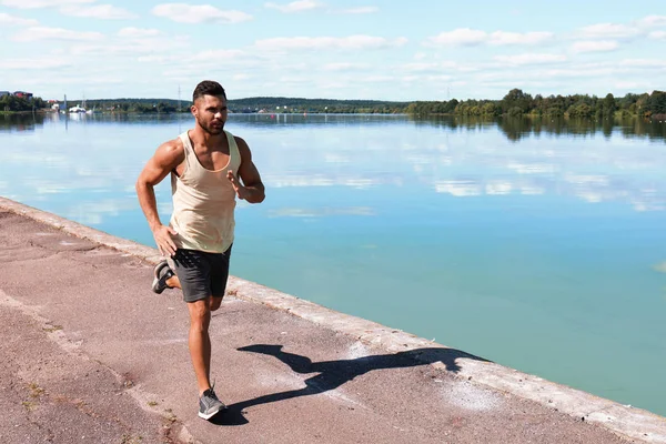 Hombre de deporte fuerte trotando mientras hace ejercicio cerca de la ribera de la ciudad — Foto de Stock