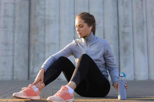 Beautiful young woman in sports clothing drinking water after sport exercise outdoors