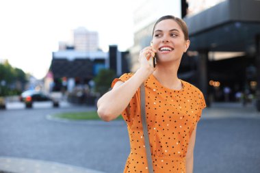 Genç gülümseyen güzel kadın telefonla konuşuyor, sokakta yürüyor