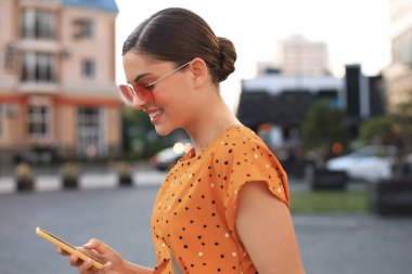 Sarı elbiseli portre moda kadın sokakta yürüyüş ve elinde akıllı telefon tutarak