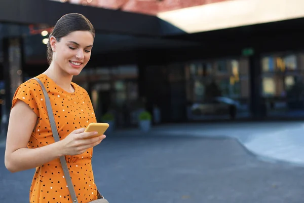 Portré divat nő sárga ruhában séta az utcán és a gazdaság okostelefon a kezében — Stock Fotó