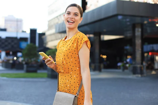 Portré divat nő sárga ruhában séta az utcán és a gazdaság okostelefon a kezében — Stock Fotó