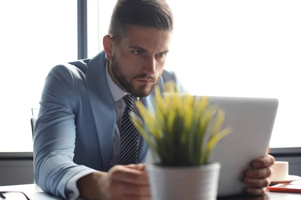 Goed uitziende zakelijke man houdt laptop terwijl zittend in het kantoor — Stockfoto