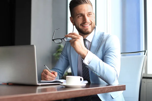 Retrato de hombre de negocios feliz sentado en el escritorio de la oficina, mirando a la cámara, sonriendo — Foto de Stock