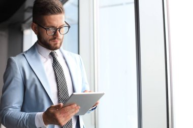 Ofiste pencerenin yanında dururken dijital tablet kullanarak formalwear modern iş adamı
