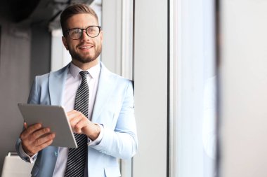 Ofiste pencerenin yanında dururken dijital tablet kullanarak formalwear modern iş adamı