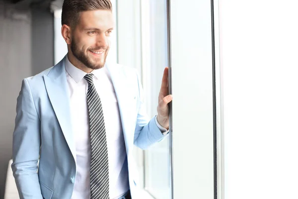 Hombre de negocios moderno en ropa formal de pie cerca de la ventana en la oficina — Foto de Stock