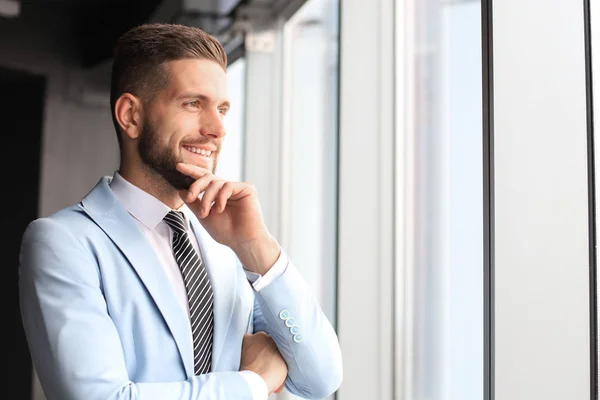 Hombre de negocios moderno en ropa formal de pie cerca de la ventana en la oficina —  Fotos de Stock