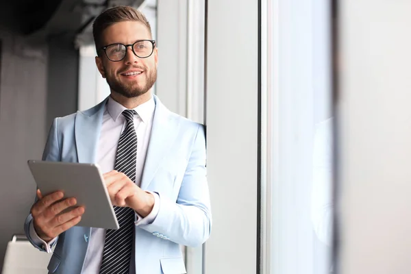 Moderne zakelijke man in formalwear met behulp van digitale Tablet terwijl staande in de buurt van venster in het kantoor — Stockfoto