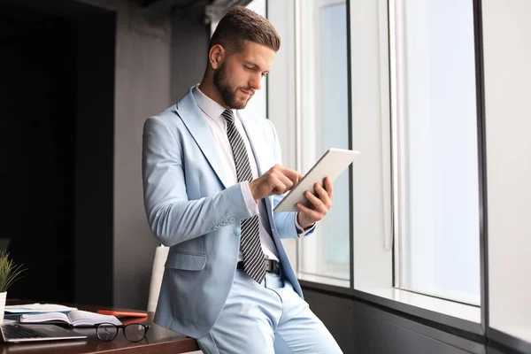 Mladý moderní podnikatel pracující pomocí digitálního tabletu, zatímco sedí v kanceláři — Stock fotografie