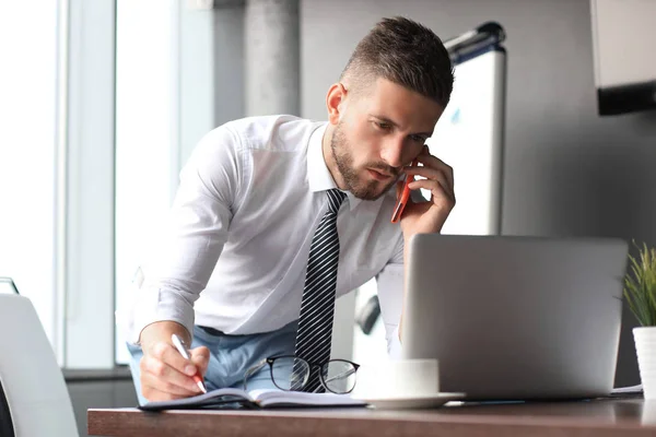 Goed uitziende jonge zakelijke man praten op de smartphone terwijl zittend in het kantoor — Stockfoto