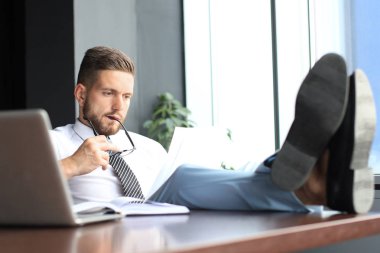 Yakışıklı işadamı masada bacakları ile oturan ve ofiste belgeleri sınav