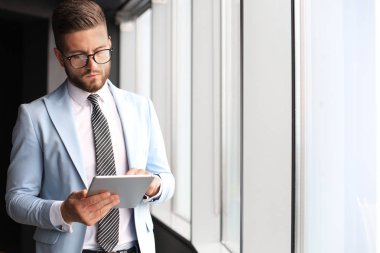 Ofiste pencerenin yanında dururken dijital tablet kullanarak formalwear modern iş adamı