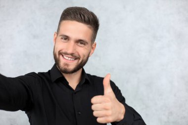 Gri arka planda izole bir şekilde duran neşeli ve yakışıklı genç adamın fotoğrafı.