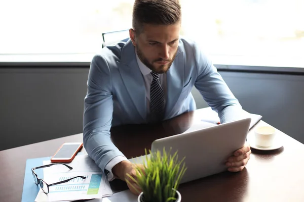 Dobrze wyglądający człowiek biznesu trzyma laptopa siedząc w biurze — Zdjęcie stockowe