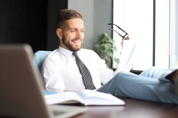 Stilig affärsman sitter med ben på bordet och examing dokument i Office — Stockfoto